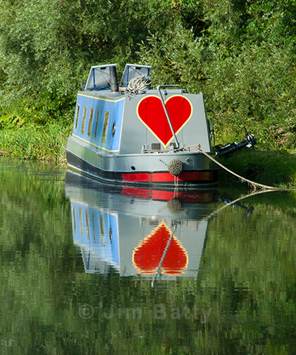Large red heart painted on the back of a narrowboat reflected in the water.