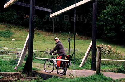 On the road photographing the Inland Waterways Man beside fully loaded touring bicycle standing on a canal lift-bridge looking back at the viewer.