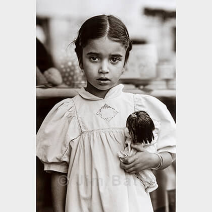 Young girl in hand-stitched dress holding a doll while standing before a shop window, Brittany, France